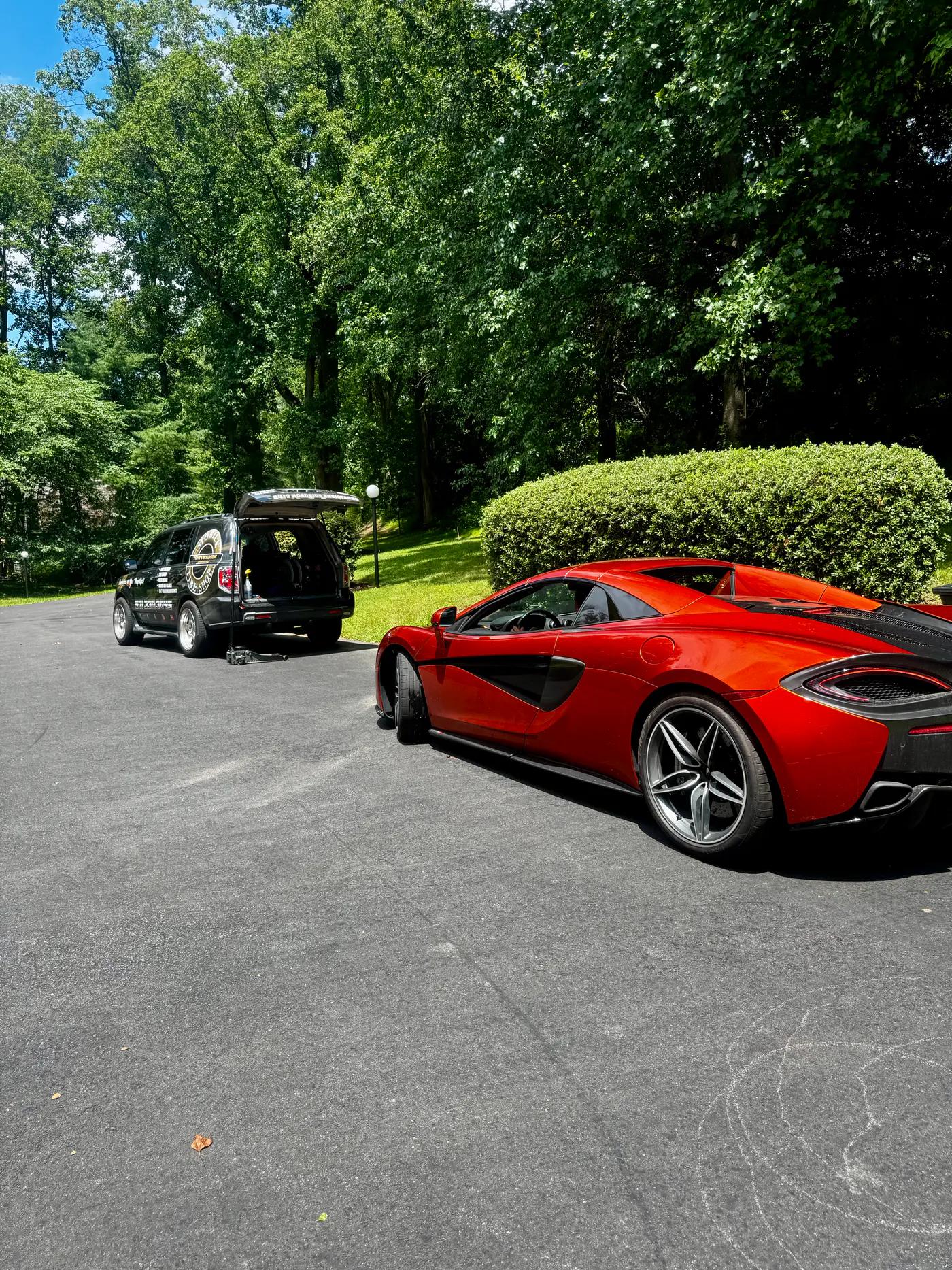 Red McLaren parked beside a TRS mobile tire service truck at a home